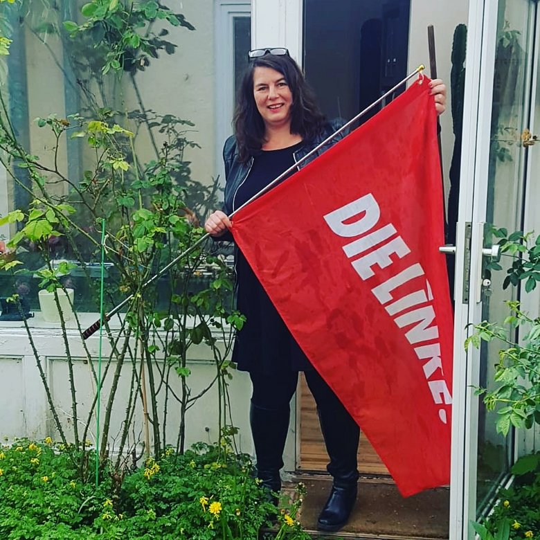Katjana Zunft steht vor einer Terassentür mit einer Linken-Fahne in der Hand